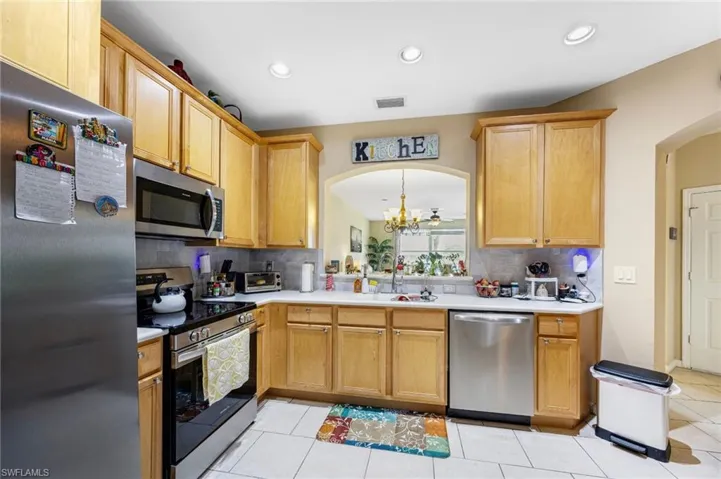 Kitchen featuring stainless steel appliances, light countertops, arched walkways, light tile patterned flooring, and backsplash