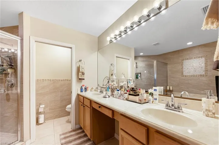 Full bathroom with tile walls, light tile patterned flooring, a shower stall, and double vanity