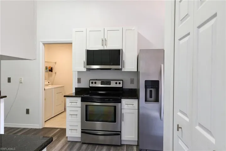 Kitchen with stainless steel appliances, white cabinets, washer and clothes dryer, and dark stone countertops