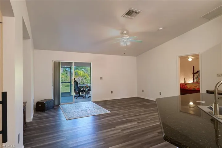 Living room featuring lofted ceiling, dark wood-style flooring, a desk, and a ceiling fan