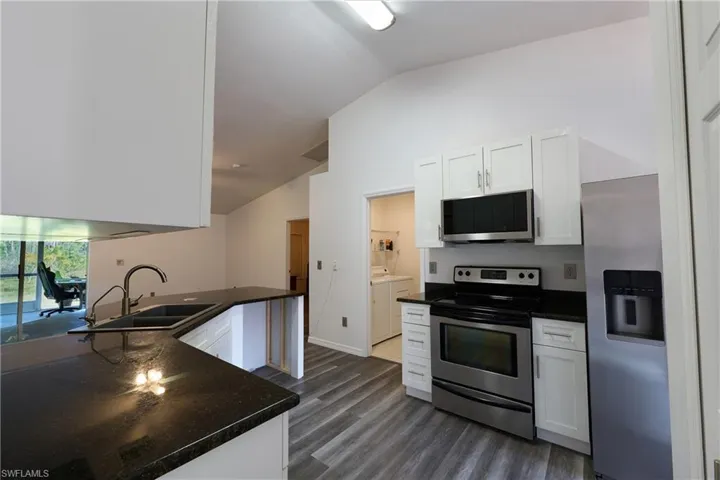 Kitchen with appliances with stainless steel finishes, white cabinets, vaulted ceiling, dark wood-style floors, and dark stone countertops