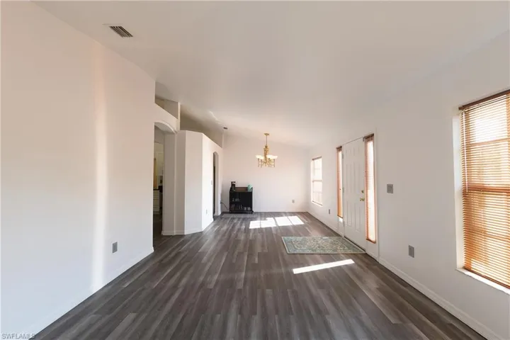Unfurnished living room featuring arched walkways, dark wood-style flooring, and a chandelier