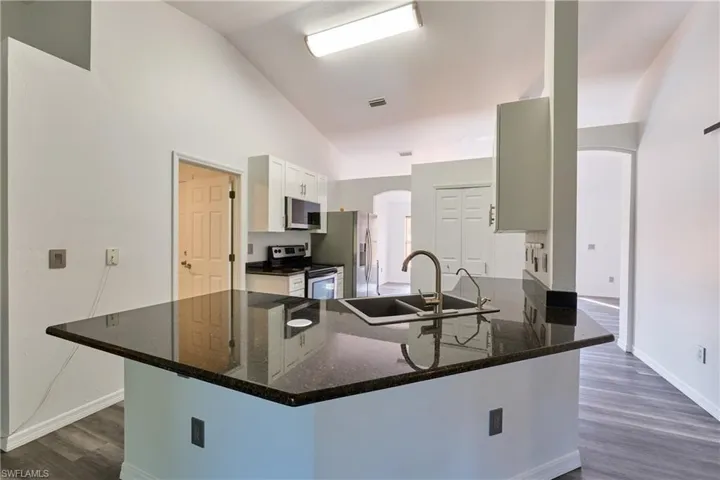 Kitchen with arched walkways, vaulted ceiling, stainless steel appliances, a peninsula, and dark stone countertops