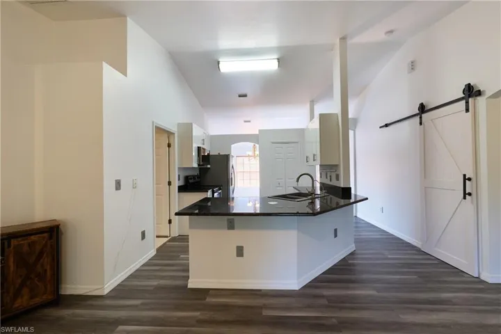 Kitchen with a barn door, dark wood-style flooring, range with electric stovetop, stainless steel microwave, and high vaulted ceiling