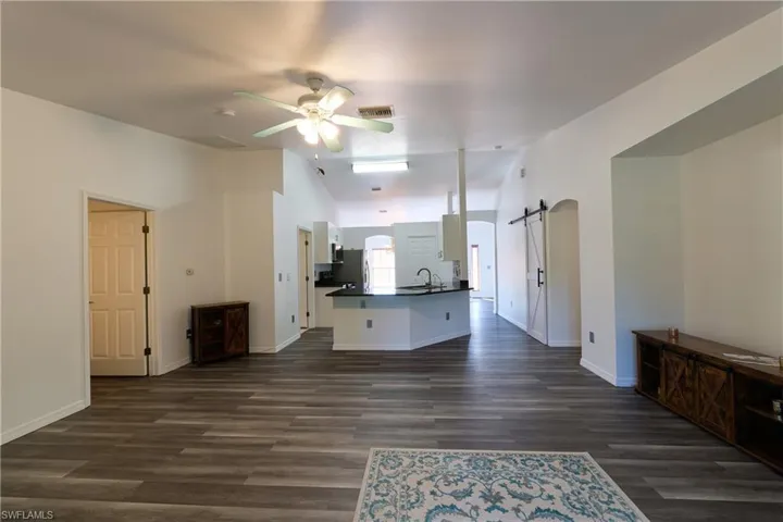 Unfurnished living room featuring a barn door, vaulted ceiling, dark wood-style floors, and ceiling fan