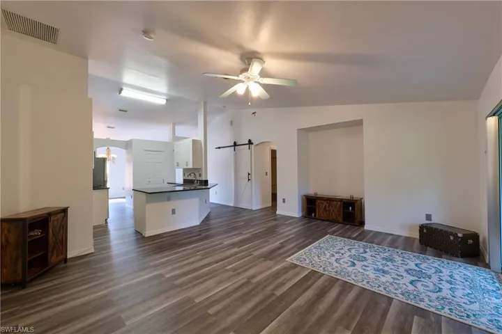 Unfurnished living room featuring a barn door, vaulted ceiling, a ceiling fan, dark wood finished floors, and arched walkways