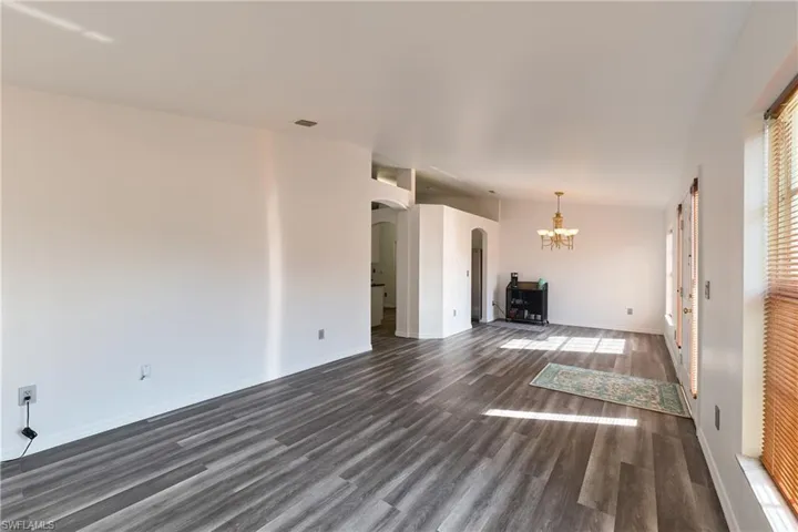 Unfurnished living room with arched walkways, a chandelier, and dark wood-type flooring