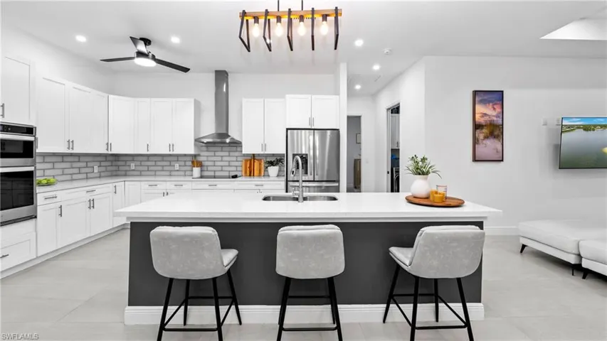 Kitchen with a center island with sink, stainless steel appliances, light stone counters, and white cabinets
