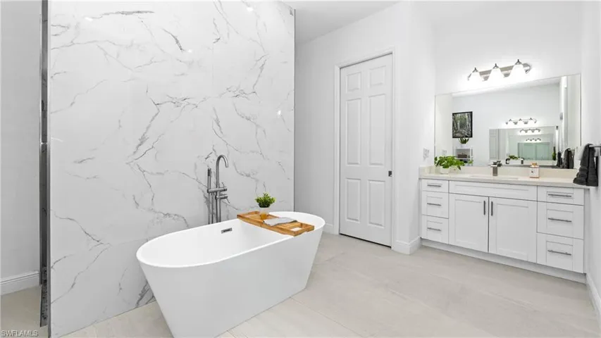 Bathroom featuring vanity, a freestanding tub, tile walls, and stone wall