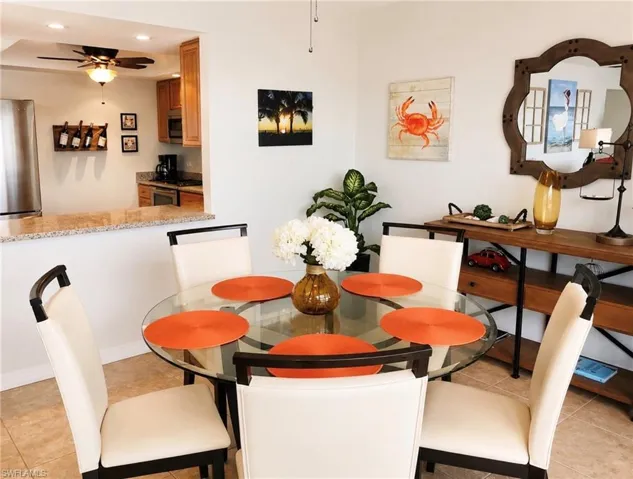 Open-concept dining area featuring tile flooring, a half wall with a granite countertop, and a pass-through opening to the kitchen with light wood cabinetry and a ceiling fan