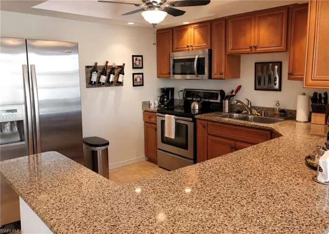 Kitchen featuring a peninsula with granite countertops, stainless steel appliances, wood cabinetry, and recessed lighting