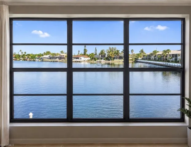 Expansive window framing water frontage with distant properties and tropical foliage