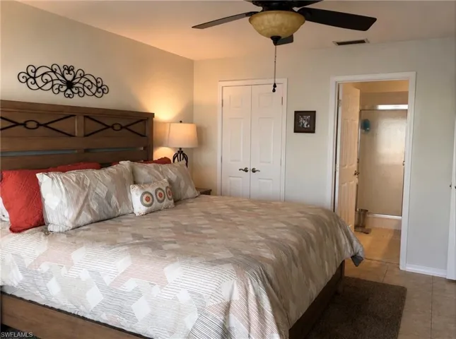 Spacious bedroom featuring light-toned walls, a ceiling fan with integrated lighting, and wood-finish flooring