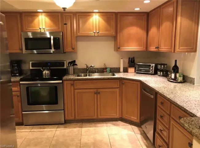 Kitchen featuring ample wood cabinetry, speckled countertops, stainless steel appliances, and tile flooring