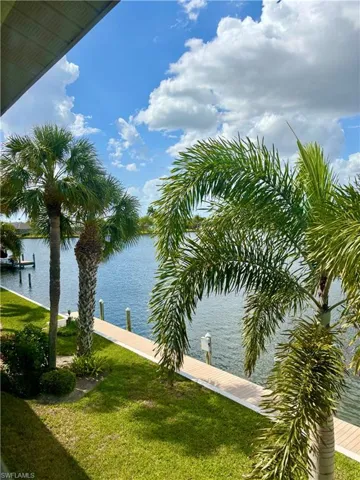 Waterfront property featuring lush green lawn, mature palm trees, and direct water access