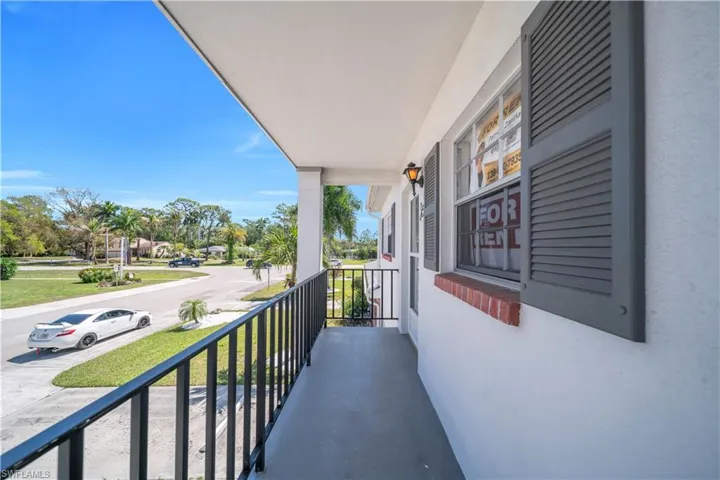 The property features a balcony with a black metal railing, offering views of the surrounding neighborhood with mature trees and a street