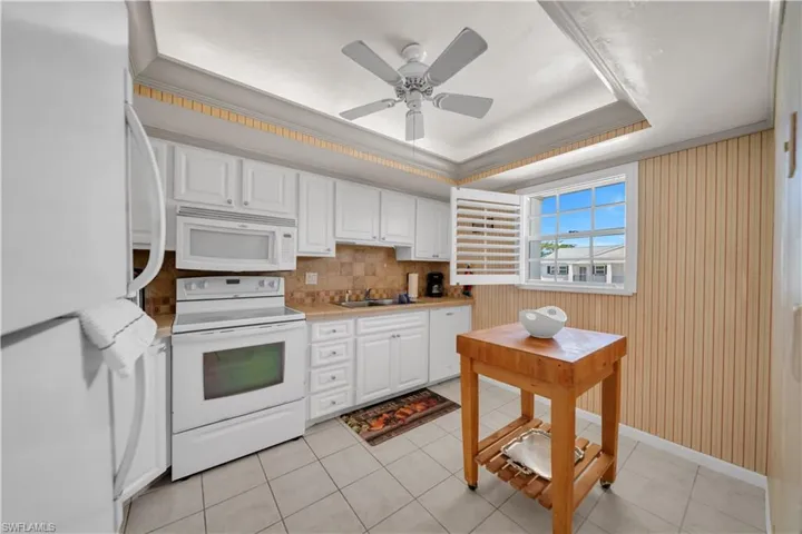 The kitchen features white cabinetry, a tiled backsplash, and a window with white shutters
