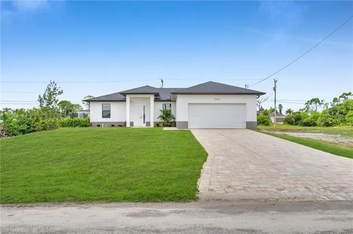 Single-story exterior featuring a light-toned stucco façade, multi-hipped roofline, integrated two-car garage, and a wide paver driveway