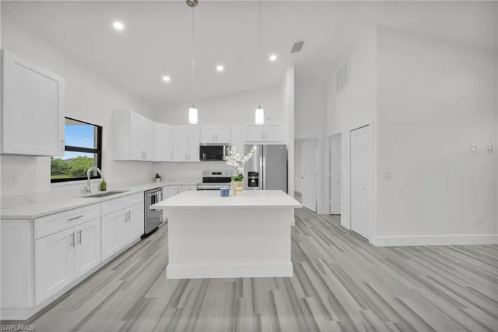 Kitchen featuring white cabinetry, quartz countertops, central island, stainless steel appliances, and wood-finish flooring under vaulted ceilings with recessed lighting
