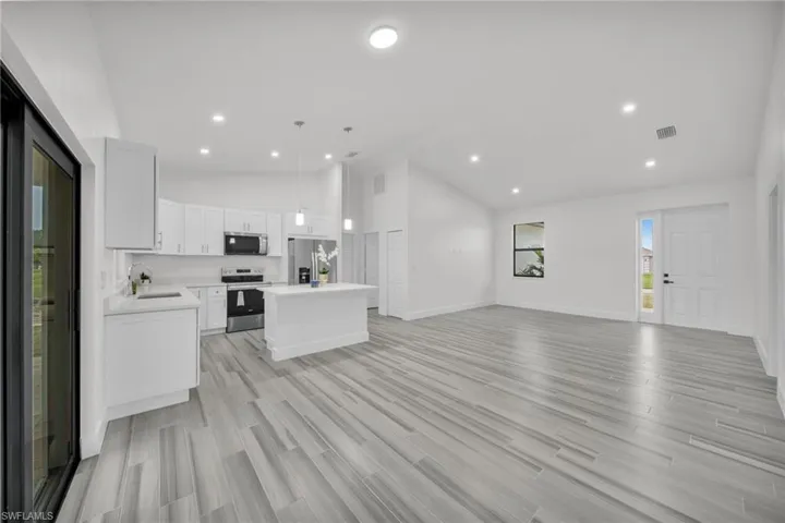 Open concept floor plan featuring vaulted ceilings, wood-finish flooring, recessed lighting, white cabinetry, and a kitchen island