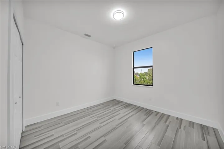 Interior room featuring wood-finish tile flooring, a single-pane window with dark trim, ceiling-mounted light fixture, and a reach-in closet with double doors