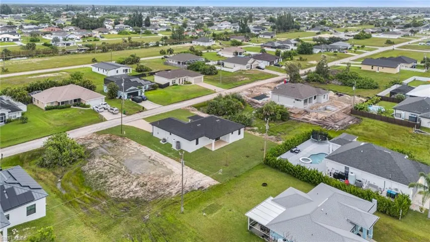 Aerial view of residential property featuring a dark-toned pitched roof, expansive lot, and surrounding suburban infrastructure