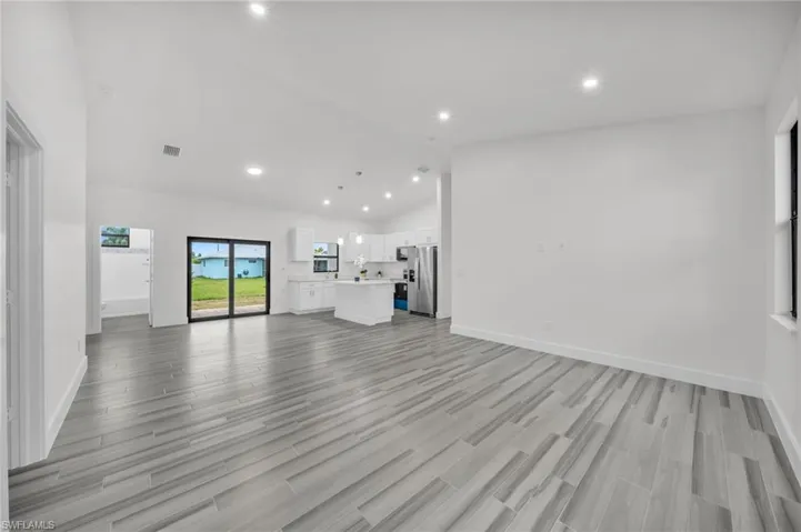 Open-concept interior featuring vaulted ceilings, wood-finish tile flooring, recessed lighting, and a kitchen equipped with white cabinetry, a center island, and stainless steel appliances