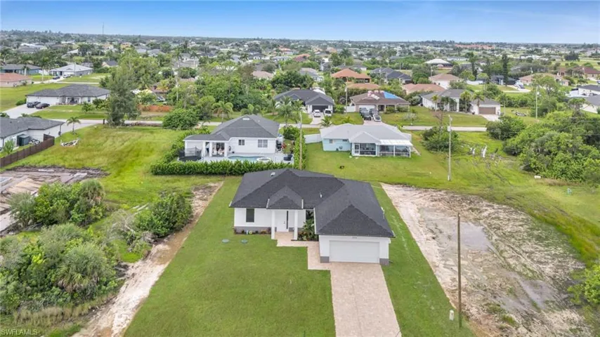Single-story residence featuring a dark shingled roof, white exterior siding, two-car garage, and a paver driveway, situated on an expansive lot