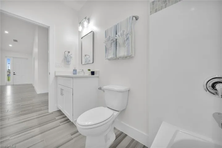 Bathroom featuring a single-sink vanity with a solid-surface countertop, wood-finish flooring, a combination tub and shower with tile surround, and recessed lighting