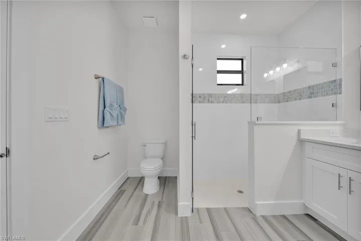Bathroom featuring wood-finish flooring, white shaker-style cabinetry, walk-in shower with glass enclosure, and decorative tile inlay