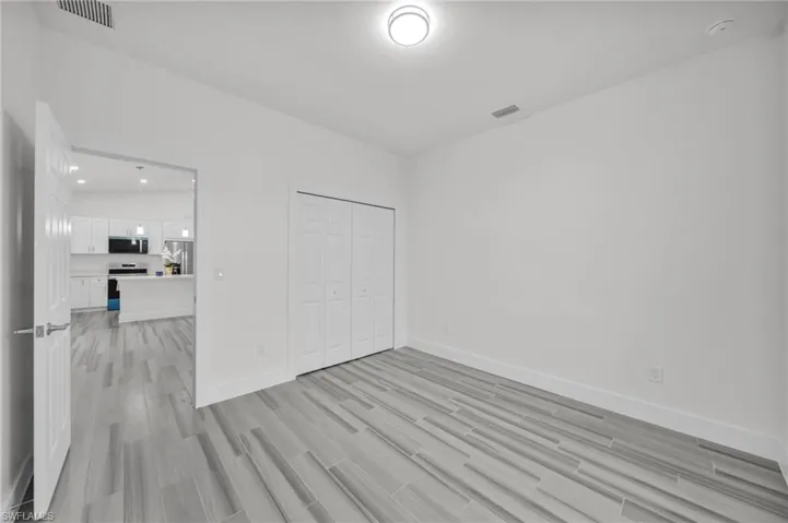 Neutral-toned wood-finish flooring, white walls, and built-in closet with four-panel folding doors