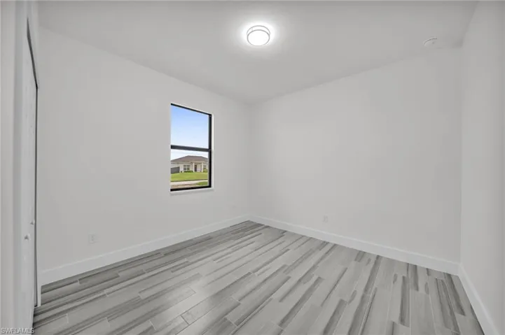 Neutral-toned wood-finish flooring, single-pane window with dark framing, flush-mount circular ceiling lighting, and a closet with bifold doors
