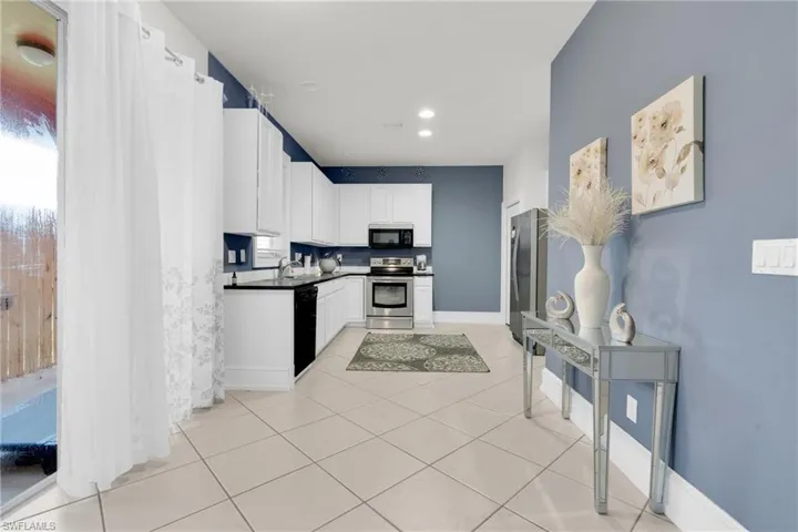 Kitchen with white cabinetry, dark countertops, light tile patterned floors, black appliances, and recessed lighting