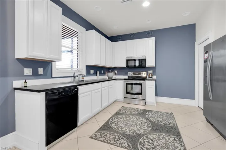 Kitchen with black appliances, dark countertops, white cabinets, light tile patterned floors, and recessed lighting