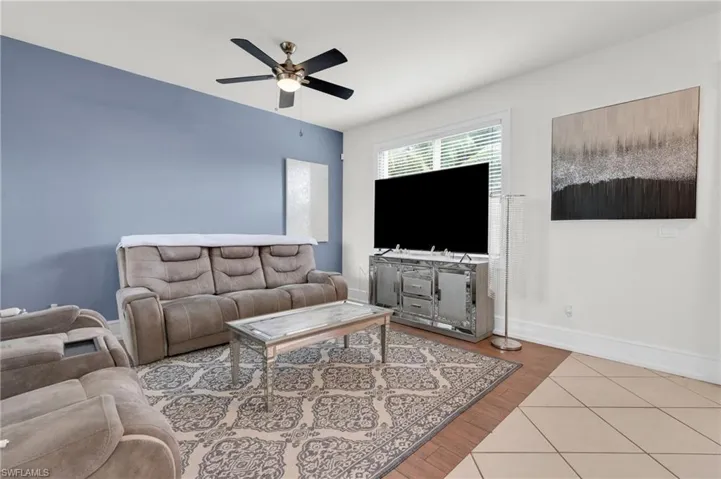 Tiled living area with a ceiling fan and baseboards