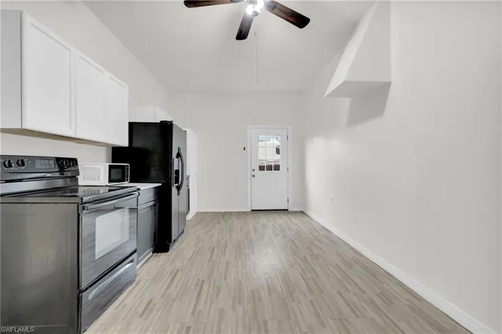 Kitchen with black range with electric cooktop, white cabinetry, light wood-style floors, a ceiling fan, and white microwave