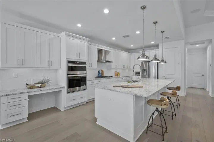 Kitchen with visible vents, wall chimney range hood, light wood-type flooring, stainless steel appliances, and white cabinetry