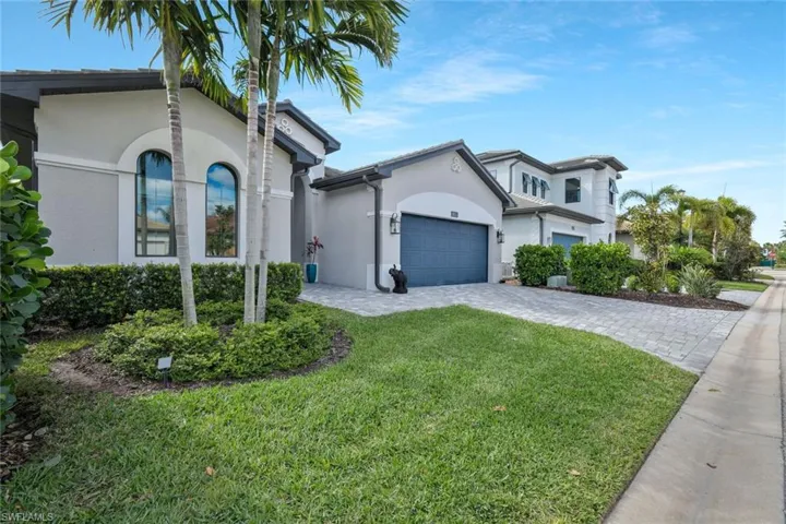 View of front of home with stucco siding, decorative driveway, a garage, and a front lawn