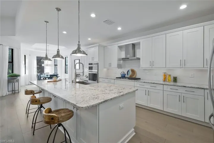 Kitchen featuring a sink, appliances with stainless steel finishes, wall chimney exhaust hood, and white cabinets