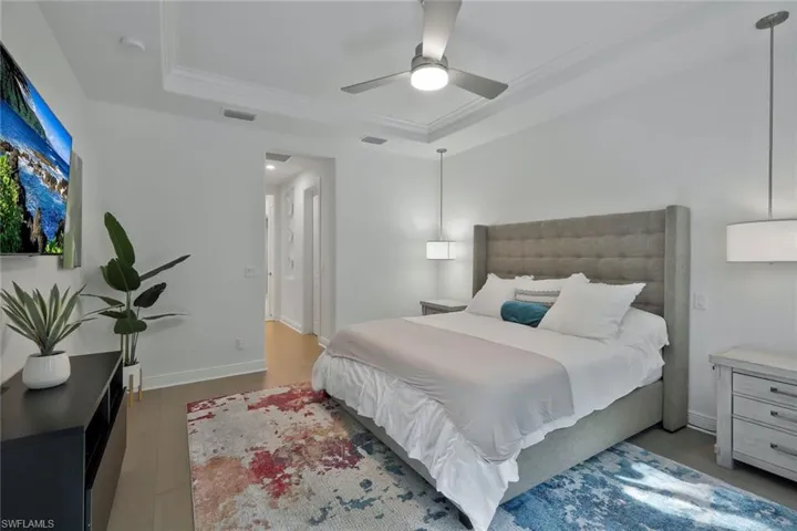 Bedroom featuring visible vents, crown molding, baseboards, a tray ceiling, and wood finished floors