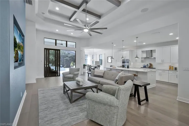 Living room with beam ceiling, coffered ceiling, baseboards, and light wood-style floors
