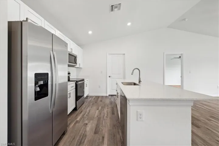 Kitchen featuring stainless steel appliances, a kitchen island with sink, wood-type flooring, white cabinets, and lofted ceiling