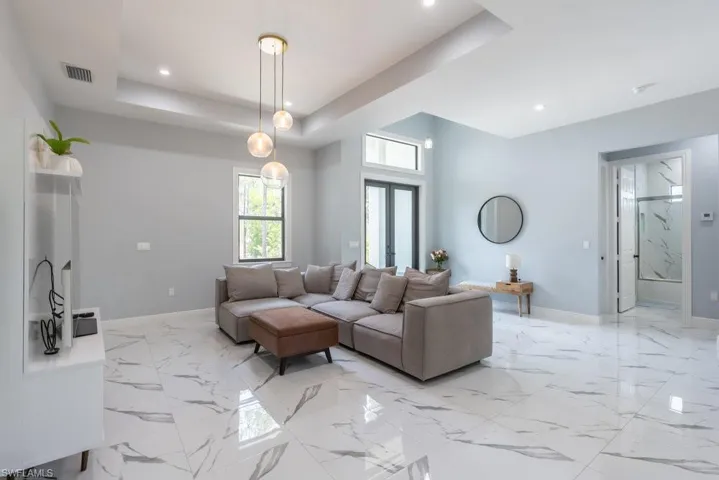 Living area featuring baseboards, a tray ceiling, recessed lighting, and light marble finish floors
