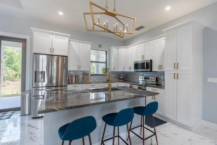 Kitchen with stainless steel appliances, a sink, light marble finish flooring, tasteful backsplash, and white cabinets