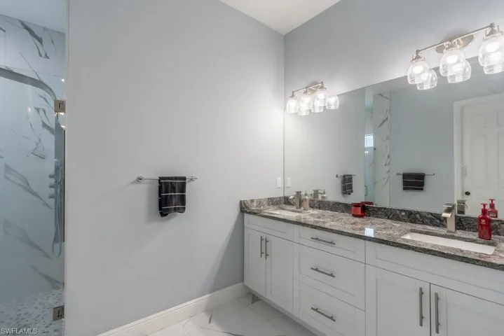 Full bath featuring marble finish flooring, a marble finish shower, baseboards, and double vanity