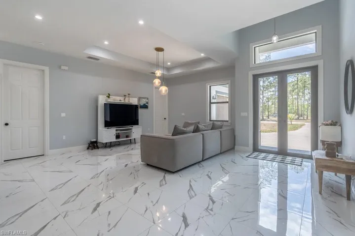 Living room with baseboards, recessed lighting, a raised ceiling, and light marble finish flooring