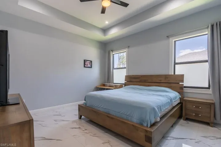 Bedroom with light marble finish floors, baseboards, recessed lighting, a tray ceiling, and a ceiling fan