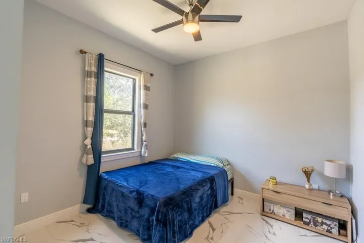 Bedroom with marble look tile flooring, baseboards, and a ceiling fan