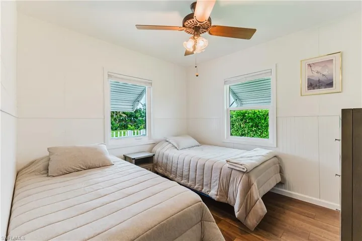 White paneled walls, wood-finish flooring, two windows, and a ceiling fan with light fixture