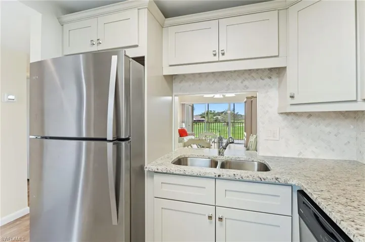 Kitchen featuring stainless steel appliances, light stone counters, decorative backsplash, sink, and white cabinetry